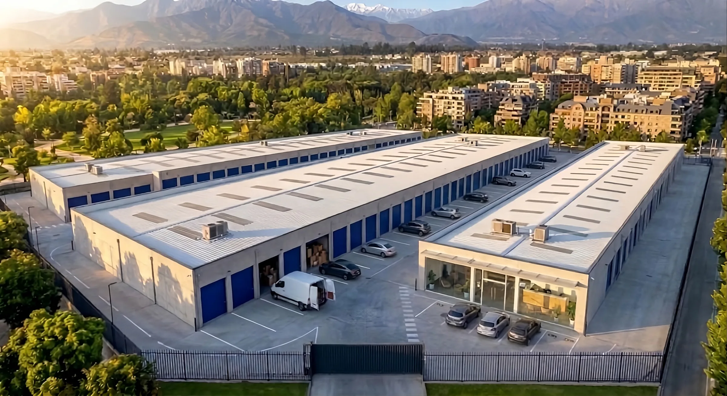 Un centro de bodegas visto desde el aire: tres edificios de puertas azules, su oficina junto al portón y la cordillera de fondo.